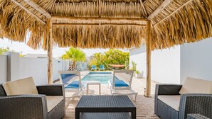 A covered outdoor area with wicker furniture, a pool, and potted plants. - Palm Beach Retreat 2 bed - 2 Bath Private (Noord)