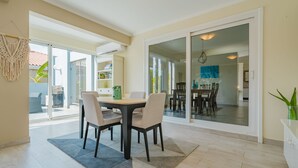 A dining area with a table and chairs, a sliding glass door leading to an outdoor space, and a view of the dining area through the glass. - Palm Beach Retreat 2 bed - 2 Bath Private (Noord)