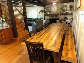 Une table à manger en bois avec des chaises, un escalier, une cheminée et une horloge au mur.