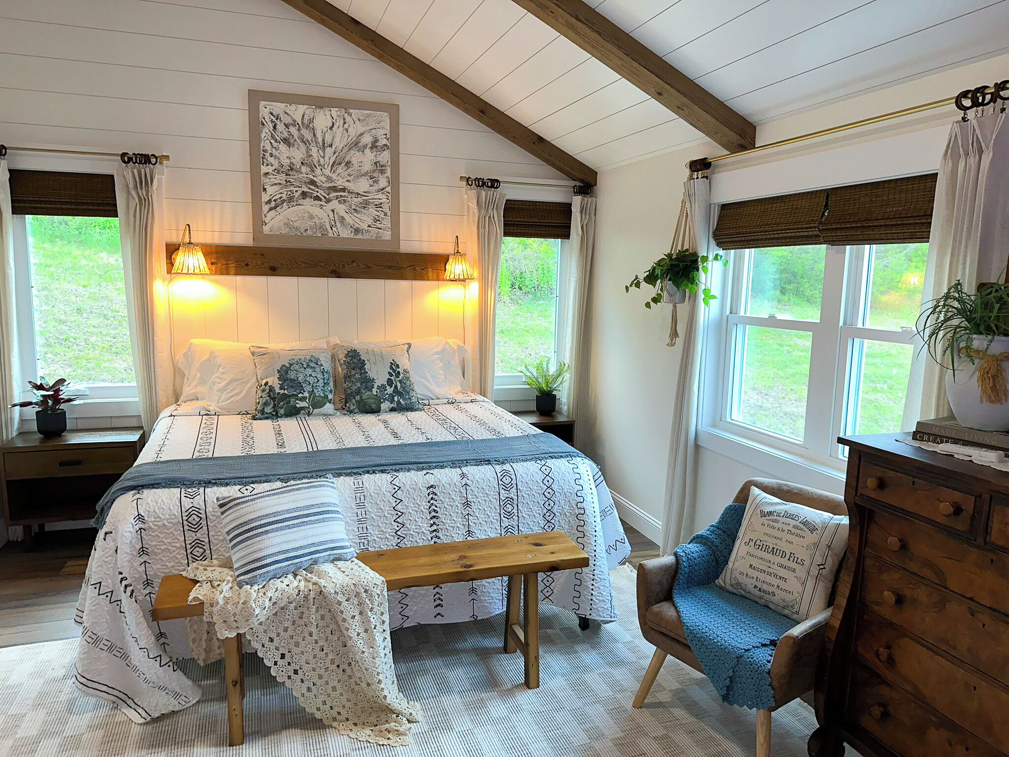 Une chambre à coucher comprenant un lit, un banc, une chaise, une commode et une fenêtre donnant sur un paysage verdoyant.