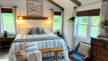 Une chambre à coucher comprenant un lit, un banc, une chaise, une commode et une fenêtre donnant sur un paysage verdoyant.