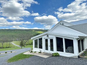 Un bâtiment blanc doté de grandes fenêtres et d’un porche abrité, se dressant sur un fond de ciel dégagé et de paysage vallonné.
