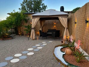 Ein überdachter Außenbereich mit einer Pergola, einem Steinweg und dekorativer Beleuchtung.