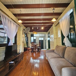 Una habitación con suelo de madera, un sofá, un televisor, un ventilador y una mesa con sillas.