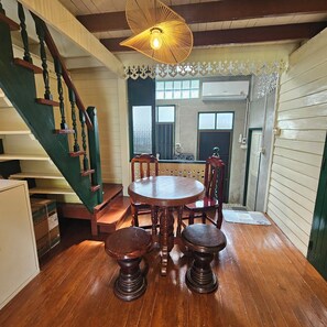 Un comedor con una mesa y sillas de madera, una escalera con barandillas verdes y una lámpara decorativa en el techo.