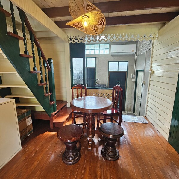 Un comedor con una mesa y sillas de madera, una escalera con barandillas verdes y una lámpara decorativa en el techo.
