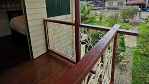 Ein Holzbalkon mit Metallgeländer, einer grünen Tür und Blick auf eine Wohngegend mit Häusern und Grünflächen.