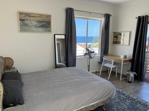 A bedroom with a bed, a desk, a chair, a standing fan, and a view of the sea. - Welcoming 4-bedroom beach house in Tamarama- Perfect for family/ friends getaway (Tamarama)