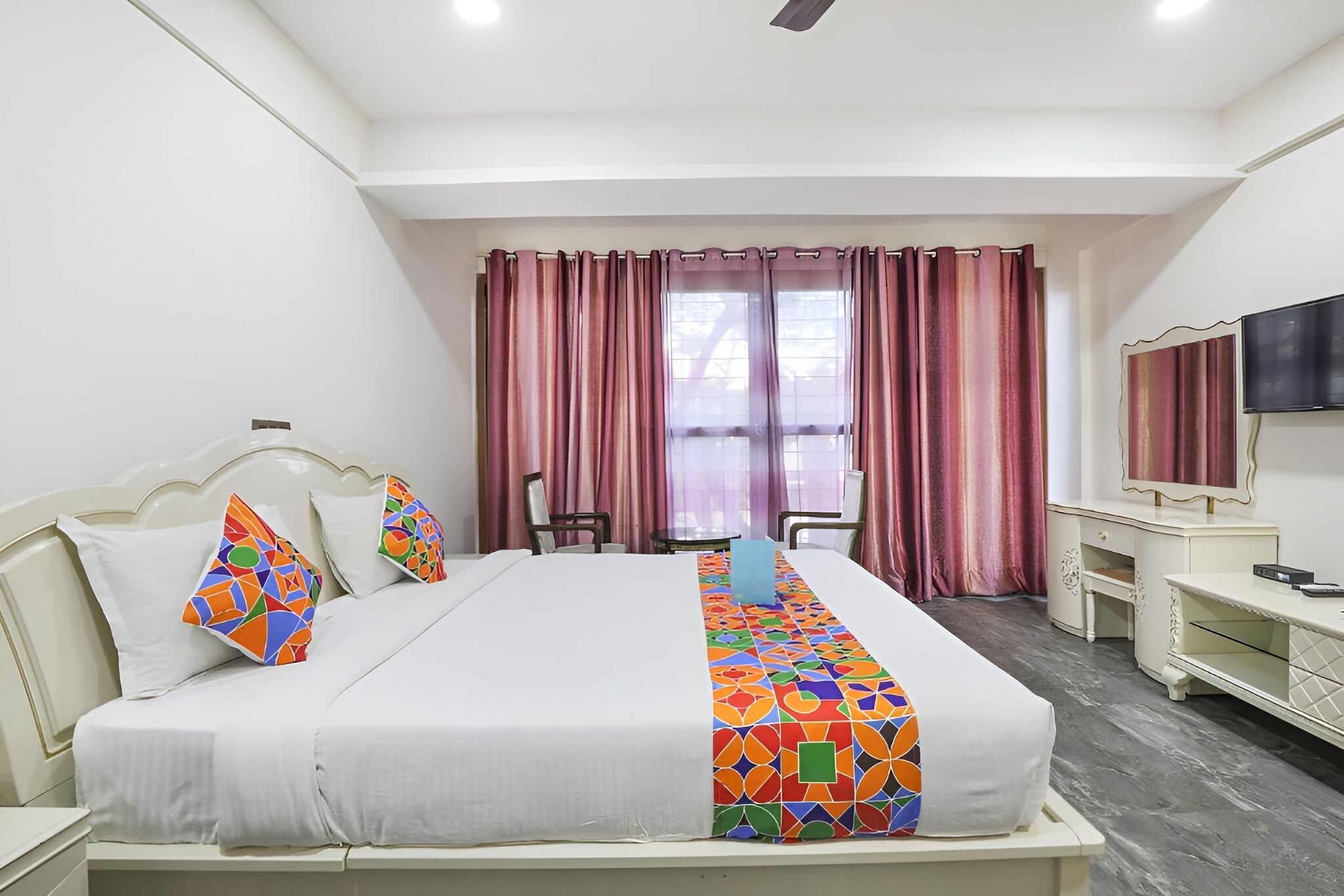 A hotel room with a bed, a desk, a chair, a TV, and a window with curtains.