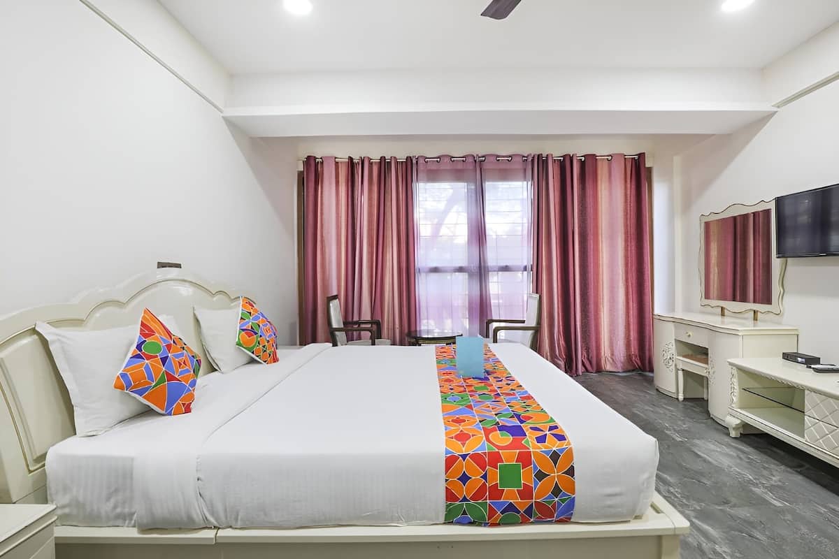 Habitación de hotel con cama, escritorio, silla, televisor y ventana con cortinas.
