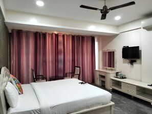 A hotel room with a bed, a desk, a chair, a television, and an air conditioning unit. - Frazer Suites (Bengaluru)