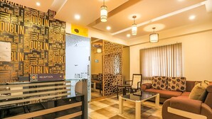 A reception area with a black and white striped counter, a reception desk, and a seating area with a sofa and a coffee table. - Frazer Suites (Bengaluru)