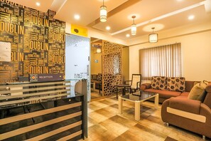 A reception area with a black and white striped counter, a reception desk, and a seating area with a sofa and a coffee table. - Frazer Suites (Bengaluru)