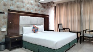A hotel room with a large bed, a nightstand, a chair, and a window with curtains. - Frazer Suites (Bengaluru)