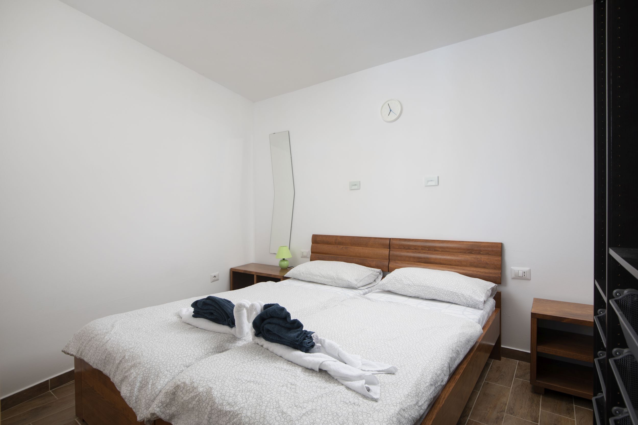 Un lit bien fait, avec une tête de lit en bois, deux tables de chevet, une horloge murale et un miroir.