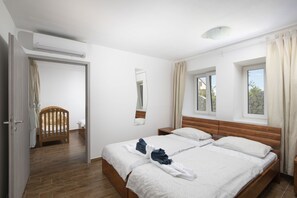 Ein Doppelbett mit weißer Bettwäsche, ein Holzkopfstück, ein Nachttisch, ein Spiegel an der Wand und ein Fenster mit Vorhängen.