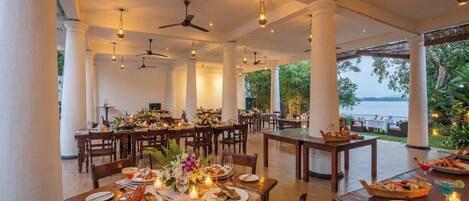 A restaurant with multiple tables, ceiling fans, and a view of the sea.