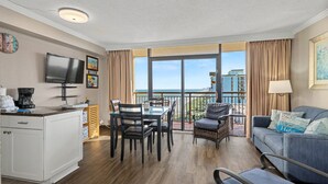 Une chambre d’hôtel avec un balcon, un coin repas, un salon et un téléviseur fixé au mur.