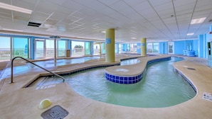 An indoor swimming pool with clear water, a lifeguard chair, and a view of the outside. - HS-0111 Ocean Front | Pool | Hot Tub | Lazy River (Myrtle Beach)