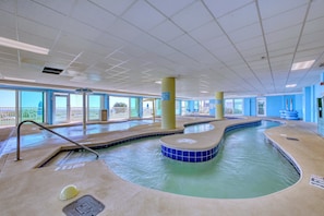 Ein Hallenbad mit klarem Wasser, einem Rettungsschwimmerstuhl und Blick ins Freie.