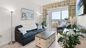 A living room with a sofa, coffee table, and a view of the sea through a balcony. - HS-0111 Ocean Front | Pool | Hot Tub | Lazy River (Myrtle Beach)