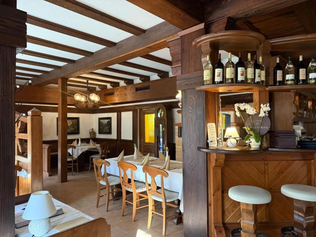 A rustic interior with wooden beams, a bar area with wine bottles, and a dining space with chairs and tables.
