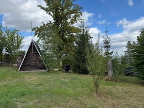 Una estructura de fusta triangular en una zona verda amb arbres i un cel serè.