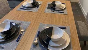 Een eettafel gedekt met borden, kommen, bestek en placematen.