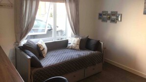 Een knus, klein vertrek met een bed, een raam met gordijnen, een radiator en een wand met ingelijste foto's.