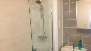 Een badkamer met een douche met glazen wand, een witte wastafel en een betegelde muur.