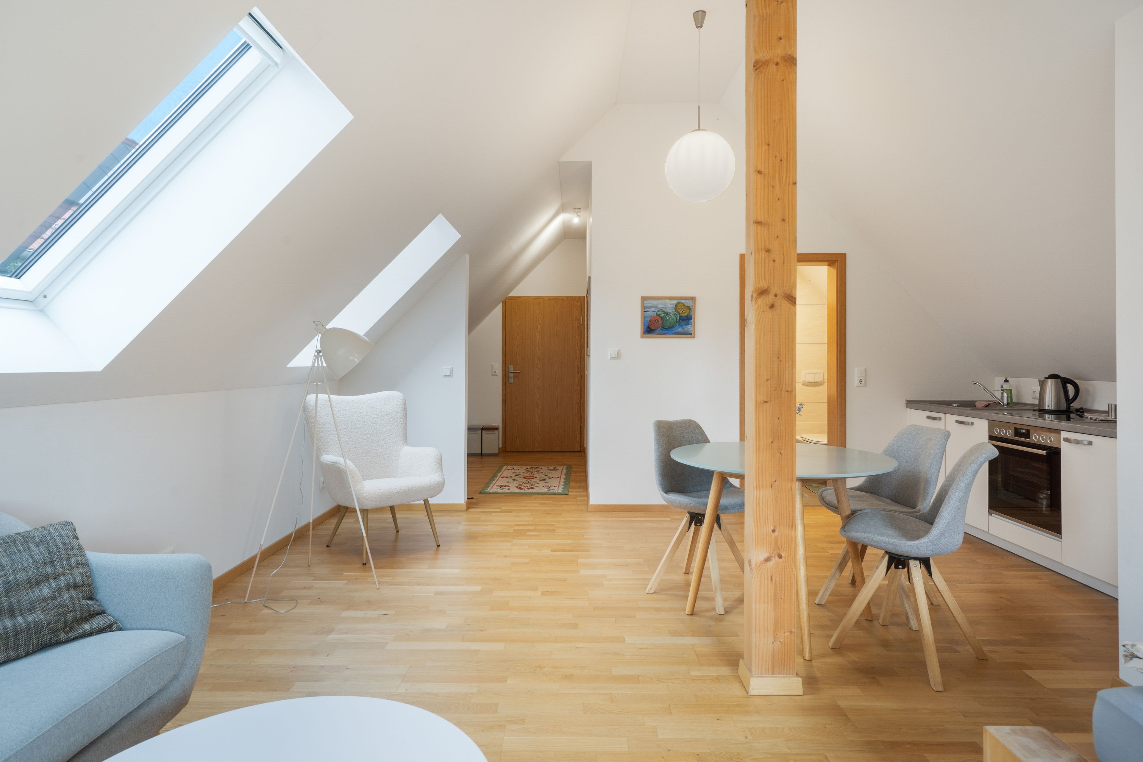 A modern interior with a skylight, a dining area with chairs, a kitchen, and a living room with a sofa.