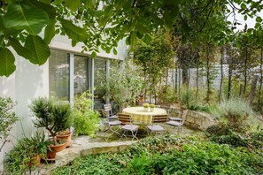 A garden patio with a round table and chairs, surrounded by potted plants and a stone wall.