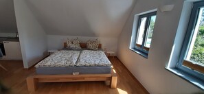 A bedroom with a bed, pillows, a bedside table, a window, and a small stool. - Apartment 'Ziegfried#Ziegenhof' (Radebeul)