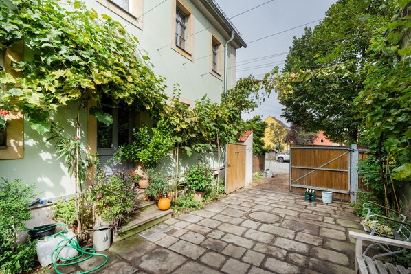 A paved courtyard with a wooden gate, potted plants, and a small pumpkin.