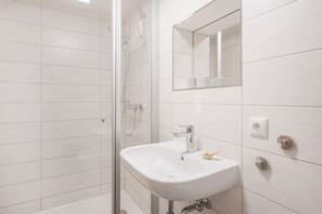 A modern bathroom with a glass shower enclosure, a white sink with a mirror above it, and a toilet with a bidet attachment.