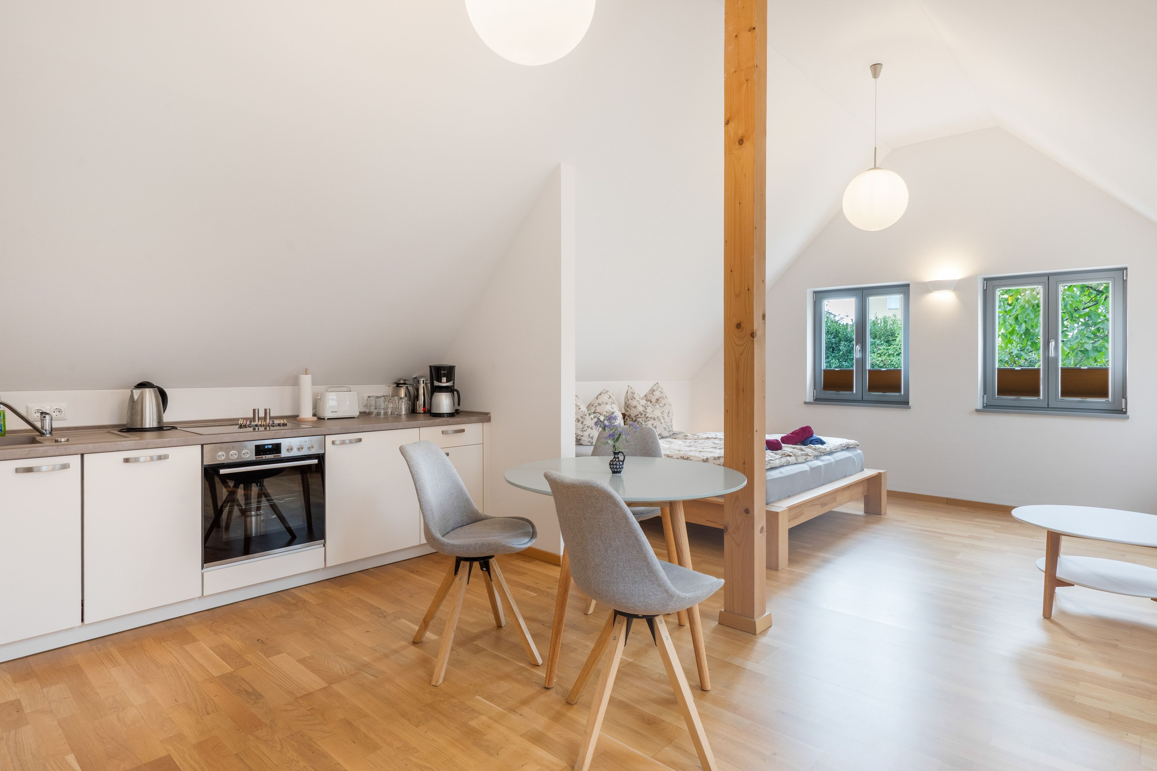 Une cuisine moderne dotée d’un four encastré, un coin repas avec une table ronde et des chaises, et une vue sur la verdure par les fenêtres.
