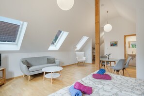 A modern loft bedroom with skylights, a sofa, a round table, and a bed with towels.