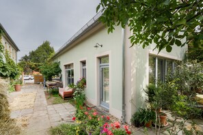 A residential building with a paved patio, a wooden table, and potted plants. - Apartment 'Ziegfried#Ziegenhof' (Radebeul)