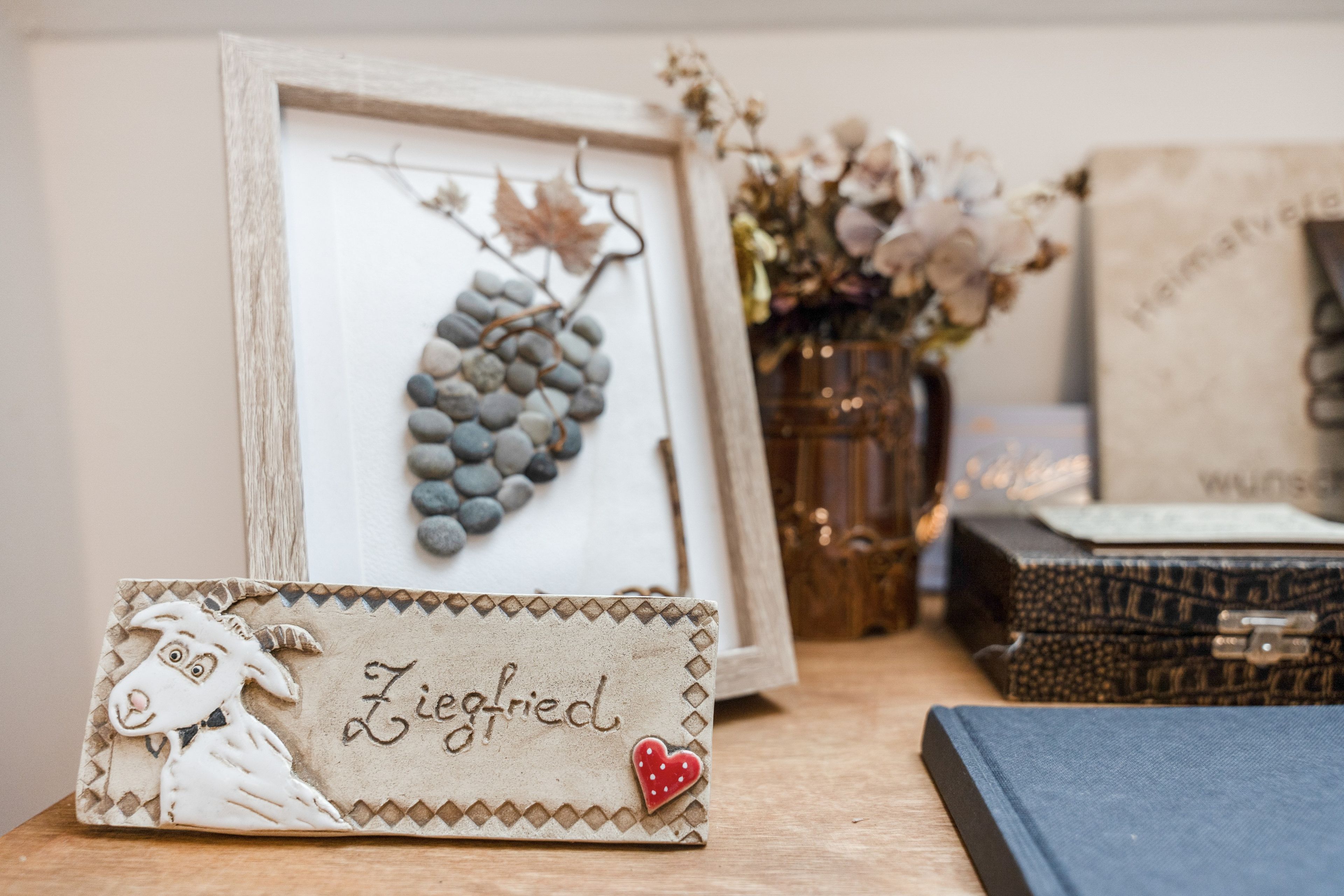 A framed artwork of a bunch of grapes, a decorative item with a name, and a vase with dried flowers.