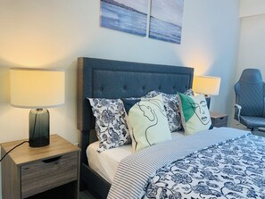 Une chambre à coucher avec un lit, deux tables de chevet, une chaise et des œuvres d’art accrochées au mur.