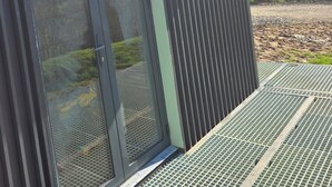 Un edificio con puerta corredera de vidrio, mosquitero metálico y reja de metal verde en la entrada.