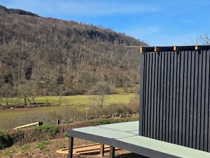 Een gebouw met een metalen dak en een groene metalen vloer, omgeven door een landelijk landschap met bomen en een heuvel.
