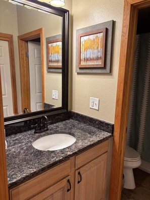 A bathroom with a granite countertop sink, wooden cabinets, a mirror, and two framed paintings on the wall. - Perfect Peace by the Lake (Keystone)