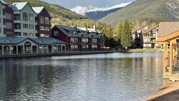A lakeside hotel with multiple buildings, a sandy beach, and mountains in the background. - Perfect Peace by the Lake (Keystone)