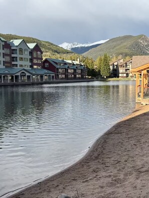 A lakeside hotel with multiple buildings, a sandy beach, and mountains in the background. - Perfect Peace by the Lake (Keystone)