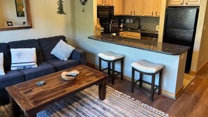 A living room with a dark-colored sofa, a wooden coffee table, and two bar stools. - Perfect Peace by the Lake (Keystone)