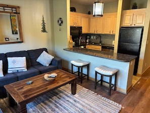 A living room with a dark-colored sofa, a wooden coffee table, and two bar stools. - Perfect Peace by the Lake (Keystone)