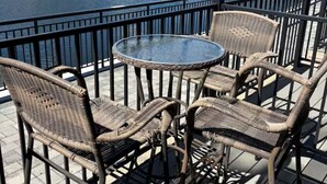 A deck with wicker chairs and a glass table overlooking a lake with buildings in the background. - Perfect Peace by the Lake (Keystone)