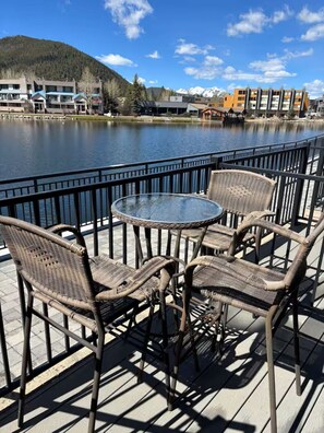 A deck with wicker chairs and a glass table overlooking a lake with buildings in the background. - Perfect Peace by the Lake (Keystone)