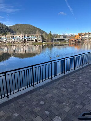 A lakeside view with a paved walkway, a metal railing, and buildings in the background. - Perfect Peace by the Lake (Keystone)